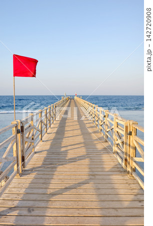 A wooden pier with a red warning flag at sunset. A wooden pier with a red warning flag at sunset. 142720908
