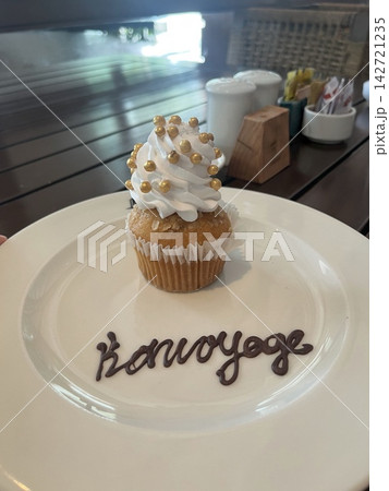 白いプレートに載るクリームと金色の粒で飾られたカップケーキとチョコ文字のメッセージ表記 白いプレートに載るクリームと金色の粒で飾られたカップケーキとチョコ文字のメッセージ表記 142721235