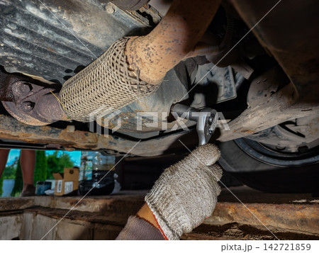 Mechanic wearing a glove using a wrench to loosen the drain plug for an oil change on a car engine undercarriage, performing vehicle maintenance. 142721859