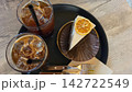カフェのテーブルに並べられたアイスコーヒーとオレンジを添えたケーキセット 142722549