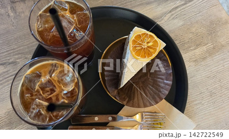 カフェのテーブルに並べられたアイスコーヒーとオレンジを添えたケーキセット カフェのテーブルに並べられたアイスコーヒーとオレンジを添えたケーキセット 142722549