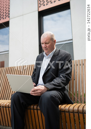 Businessman working on laptop outdoors near modern office 142722634