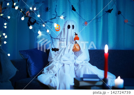 Enjoying a spooky evening in a ghost costume, embracing the playful atmosphere of a Halloween celebration, fun, entertainment, and tradition during Halloween night. 142724739