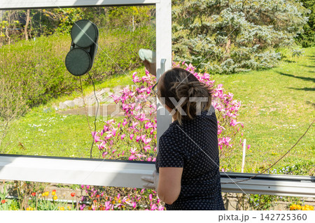 Woman cleaning large garden window on a bright sunny day Woman cleaning large garden window on a bright sunny day 142725360