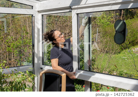 Woman cleaning greenhouse windows in bright spring garden Woman cleaning greenhouse windows in bright spring garden 142725362