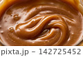 Extreme macro food photography highlighting the glossy, flowing swirl texture of rich golden caramel sauce. 142725452