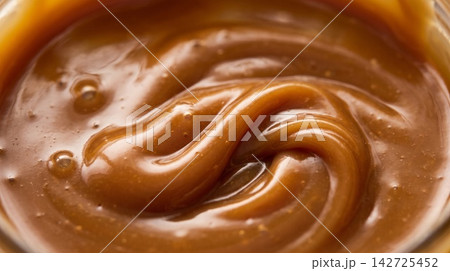 Extreme macro food photography highlighting the glossy, flowing swirl texture of rich golden caramel sauce. 142725452