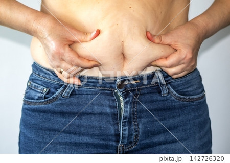 Woman pinching belly fat above jeans showing abdominal skin, body weight and health concern Woman pinching belly fat above jeans showing abdominal skin, body weight and health concern 142726320