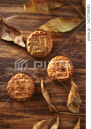 Traditional mooncakes with intricate designs placed on a wooden surface, surrounded by dried leaves, symbolizing the Mid-Autumn Festival celebration Traditional mooncakes with intricate designs placed on a wooden surface, surrounded by dried leaves, symbolizing the Mid-Autumn Festival celebration 142726683