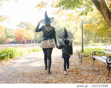 Mother and daughter walk through autumn park during Halloween celebration, enjoying colorful foliage and seasonal atmosphere while spending quality time together outdoors. 142727096
