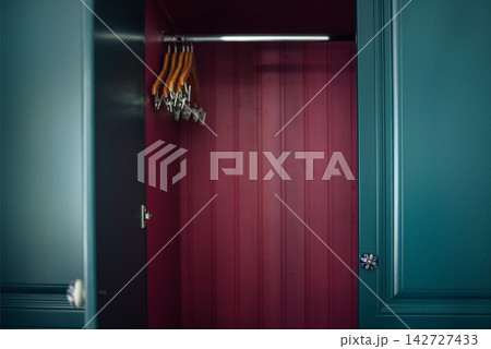 Interior view of a modern wardrobe with teal doors, featuring wooden hangers and a deep red interior, showcasing a stylish and organized storage solution Interior view of a modern wardrobe with teal doors, featuring wooden hangers and a deep red interior, showcasing a stylish and organized storage solution 142727433