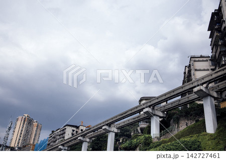 Urban landscape featuring elevated monorail system traversing through residential buildings under a cloudy sky in a modern city setting 142727461