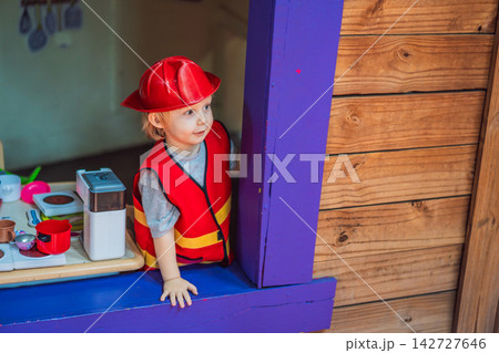 Little boy dressed as firefighter playing in a red toy fire truck at an outdoor playground with helmet safety vest pretend rescue game childhood dreams role play and near viewpoint. Little boy dressed as firefighter playing in a red toy fire truck at an outdoor playground with helmet safety vest pretend rescue game childhood dreams role play and near viewpoint. 142727646