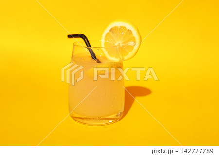 Refreshing lemonade drink in a clear glass with a lemon slice and black straw on a vibrant yellow background, perfect for summer beverage ideas and recipes Refreshing lemonade drink in a clear glass with a lemon slice and black straw on a vibrant yellow background, perfect for summer beverage ideas and recipes 142727789