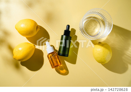 Cosmetic dropper bottles with glass of water and fresh lemon fruits in bright sunlight, clean beauty and skincare concept, top view on yellow background Cosmetic dropper bottles with glass of water and fresh lemon fruits in bright sunlight, clean beauty and skincare concept, top view on yellow background 142728628