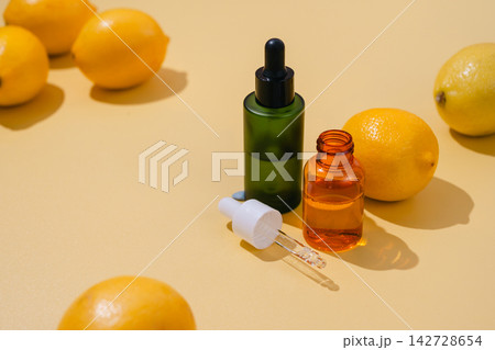 Vitamin C skincare serum in dropper bottles surrounded by fresh lemons on yellow background, bright natural beauty and antioxidant concept 142728654