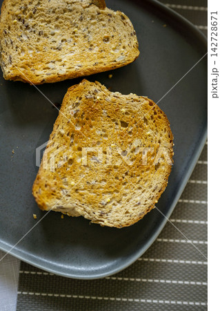 Whole grain seeded toast slices on dark plate, healthy breakfast food concept Whole grain seeded toast slices on dark plate, healthy breakfast food concept 142728671