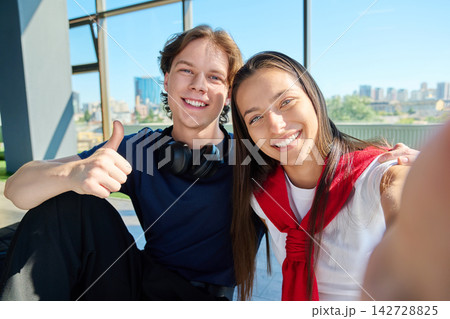 Smiling young students taking selfie and showing thumb up near big window 142728825