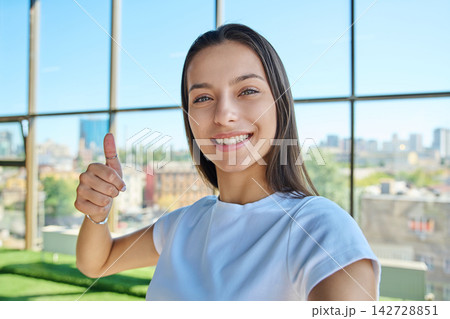 Young smiling woman showing thumb up hand sign while taking selfie photo 142728851