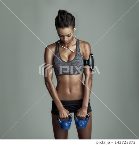 Exercise, kettlebell and woman in studio for workout with earphones, streaming kpop music and arm muscle. Weights, listening to sound and athlete girl by gray background for audio media and training 142728872