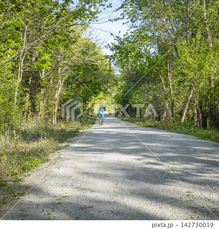 Distant male cyclist is riding a folding bike on Katy Trail near Rocheport, Missouri, spring scenery. The Katy Trail is 237 mile bike trail converted from an old railroad. 142730019