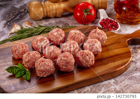 Raw meatballs on wooden cutting board with fresh basil, rosemary, garlic, tomato and peppercorns on marble countertop Raw meatballs on wooden cutting board with fresh basil, rosemary, garlic, tomato and peppercorns on marble countertop 142730793