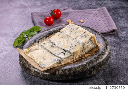 Sliced gorgonzola cheese on dark stone plate with basil leaves and cherry tomatoes 142730830