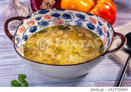 Chicken noodle soup in patterned ceramic bowl with fresh dill, garlic, and tomatoes on rustic wooden surface Chicken noodle soup in patterned ceramic bowl with fresh dill, garlic, and tomatoes on rustic wooden surface 142730864