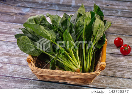 Fresh spinach leaves in woven basket on rustic wooden surface with cherry tomatoes nearby, natural lighting and shallow depth of field Fresh spinach leaves in woven basket on rustic wooden surface with cherry tomatoes nearby, natural lighting and shallow depth of field 142730877