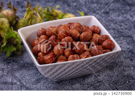 Hazelnuts in white textured bowl with green husks on dark stone surface, warm brown tones and shallow depth of field Hazelnuts in white textured bowl with green husks on dark stone surface, warm brown tones and shallow depth of field 142730900