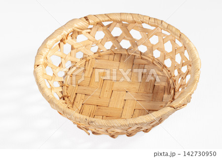 Handwoven bamboo basket with open lattice sides and tight woven base, isolated on white background, natural tan color, shallow depth of field 142730950