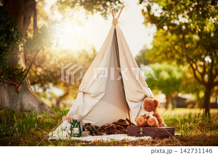 Teepee, tent and fun in garden in nature outdoor at park for playing, camp and imagination of adventure. Cloth, shelter and fantasy house for background in forest with blanket, suitcase or teddy bear 142731146