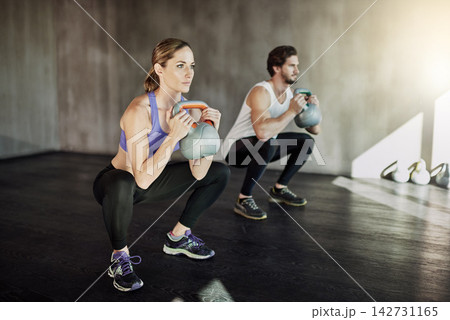Workout, squat and couple in gym with kettlebell, power training and fitness challenge together at sports club. Man, woman or personal trainer with muscle development, healthy body and exercise. 142731165
