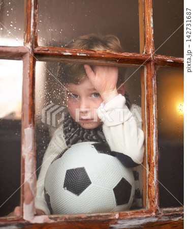 Portrait, depressed and sad child by window with anxiety for bullying trauma, soccer ball and scared with stress. Orphan, football and young boy by glass for lonely and adoption conflict in Ireland 142731687