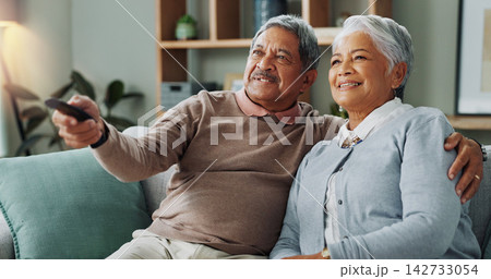 Senior, couple and watching tv in home to relax with happiness on vacation or holiday in retirement. Elderly, man and woman hug on sofa and click choice for streaming comedy movies, series or film 142733054