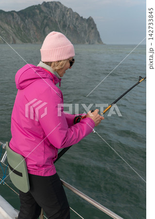 Woman fishes from a boat near rugged Kamchatka coastline. Sea trip, marine travel, recreational fishing, outdoor leisure, active journey, adventure tourism and scenic exploration. Woman fishes from a boat near rugged Kamchatka coastline. Sea trip, marine travel, recreational fishing, outdoor leisure, active journey, adventure tourism and scenic exploration. 142733845
