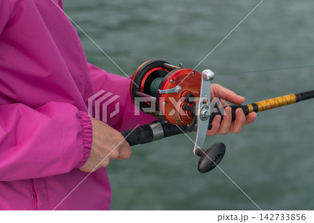Close-up of hands holding fishing rod with reel during sea fishing trip. Recreational fishing, angling equipment, outdoor leisure, active travel, marine adventure and sport fishing 142733856