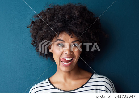 Portrait, emoji and tongue with funny face in studio for fun, relax and playful attitude on blue background. Lady, comic and goofy black woman with facial expression, crazy and personality isolated 142733947