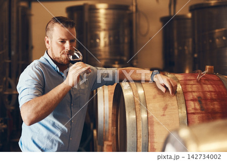 Glass, taste and test with man in wine cellar for industry, manufacturing or production. Barrel, business and storage with sommelier drinking alcohol at winery for distillation or fermentation Glass, taste and test with man in wine cellar for industry, manufacturing or production. Barrel, business and storage with sommelier drinking alcohol at winery for distillation or fermentation 142734002