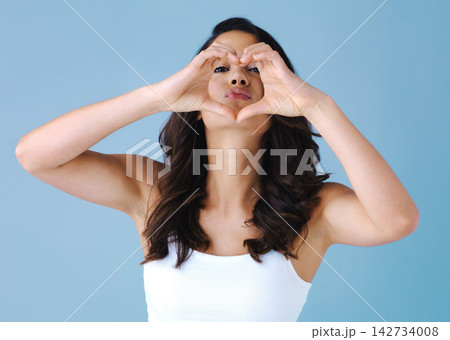 Woman, beauty and heart hands in studio portrait with choice for salon by blue background. Girl, model or person with icon, sign and emoji for symbol with pout lips, review or decision with hair care 142734008