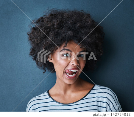 Black woman, emoji and tongue with facial expression in studio for fun, relax and playful attitude on blue background. Lady, comic and goofy portrait with a funny face, crazy and personality isolated Black woman, emoji and tongue with facial expression in studio for fun, relax and playful attitude on blue background. Lady, comic and goofy portrait with a funny face, crazy and personality isolated 142734012
