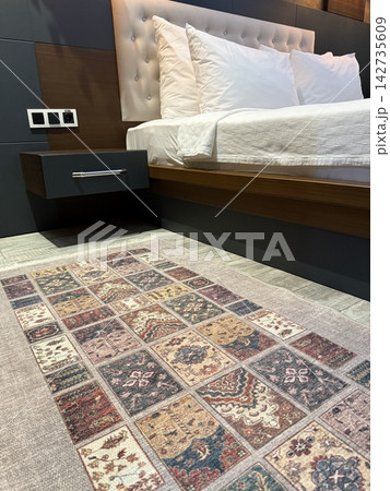 Modern bedroom with upholstered headboard, white bedding, wooden panels, and patterned area rug Modern bedroom with upholstered headboard, white bedding, wooden panels, and patterned area rug 142735609