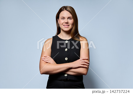 Smiling businesswoman standing with arms crossed on light blue background Smiling businesswoman standing with arms crossed on light blue background 142737224
