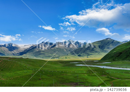 Vast Green Grassland with Winding River and Majestic Mountains under Blue Sky Vast Green Grassland with Winding River and Majestic Mountains under Blue Sky 142739036