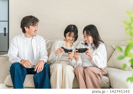 ゲーム機で遊びながら笑顔で盛り上がる家族3人。親子で楽しむ休日の団らん ゲーム機で遊びながら笑顔で盛り上がる家族3人。親子で楽しむ休日の団らん 142741143