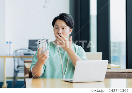 オフィスでスマホを使って驚く若いエンジニア オフィスでスマホを使って驚く若いエンジニア 142741365