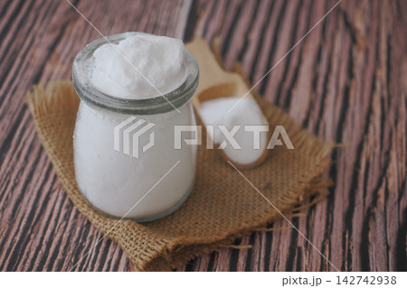 A glass jar holds a baking soda powder on a burlap cloth and wooden spoon A glass jar holds a baking soda powder on a burlap cloth and wooden spoon 142742938