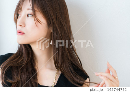 長い髪に触れながら横を見つめる女性。美髪とヘアケアをイメージした美容素材 長い髪に触れながら横を見つめる女性。美髪とヘアケアをイメージした美容素材 142744752