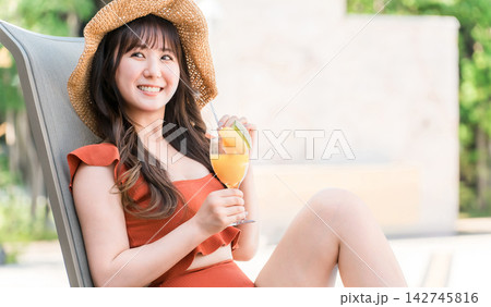 プールサイドでトロピカルドリンクを楽しむ水着姿の女性。夏のリゾート旅行とバカンス プールサイドでトロピカルドリンクを楽しむ水着姿の女性。夏のリゾート旅行とバカンス 142745816