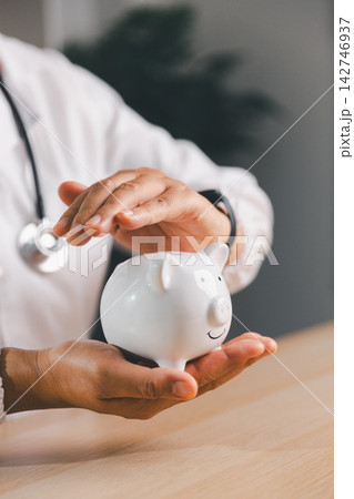 Healthcare professional holding and protecting a white piggy bank, representing medical savings, health insurance, financial security, emergency funds, budgeting, and planning for healthcare costs. 142746937